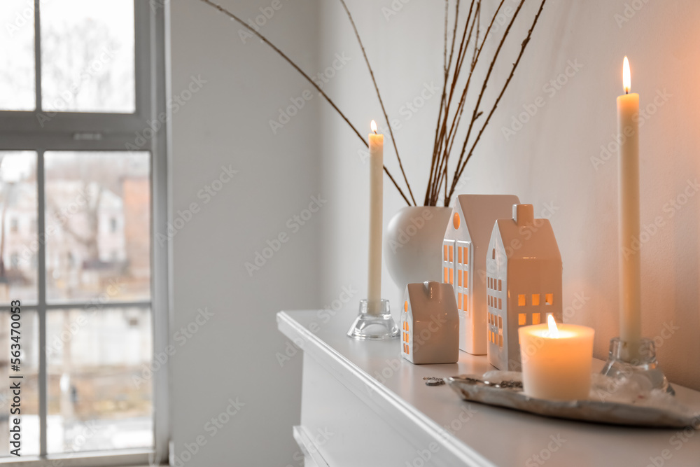 House candle holders and vase with tree branches on mantelpiece near light wall