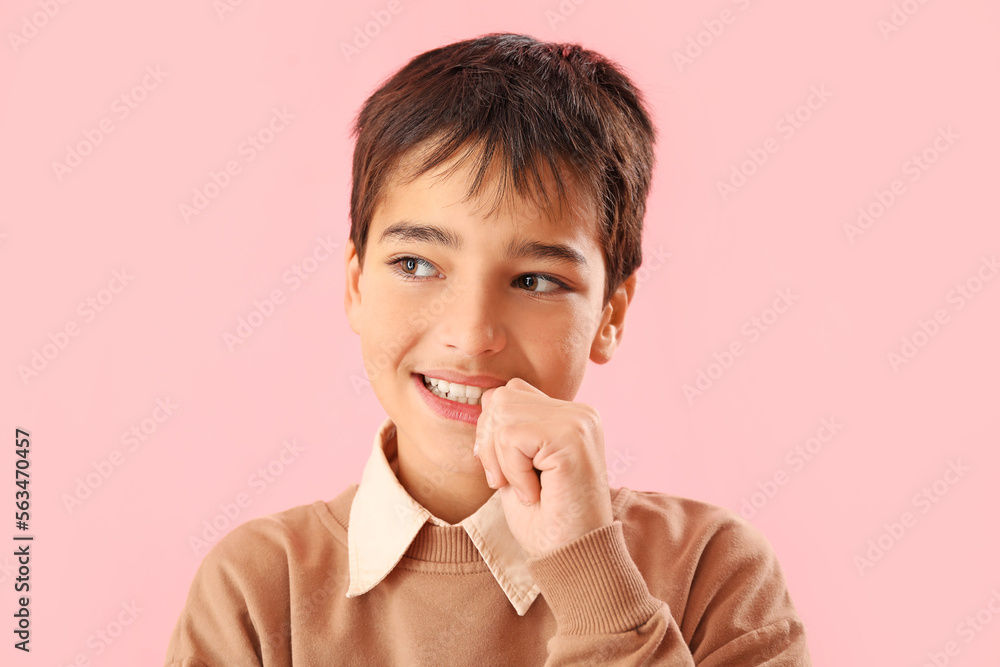 Little boy biting nails on pink background, closeup