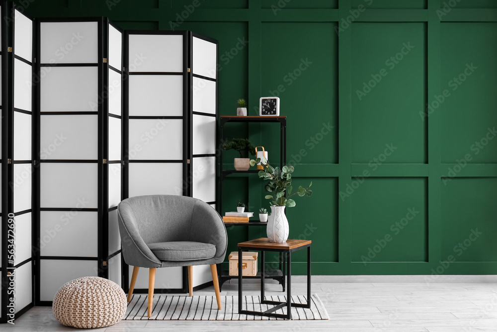 Interior of room with folding screen, armchair and pouf near green wall