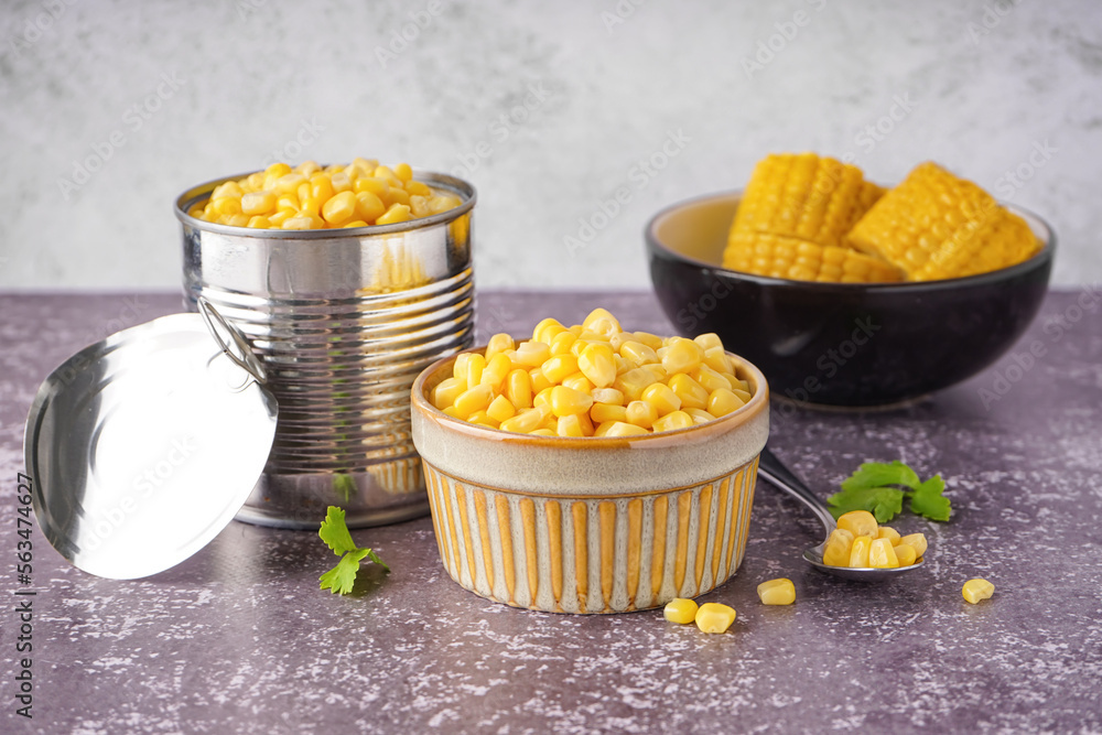 Bowls with corn kernels and cobs, tin can and parsley leaves on table