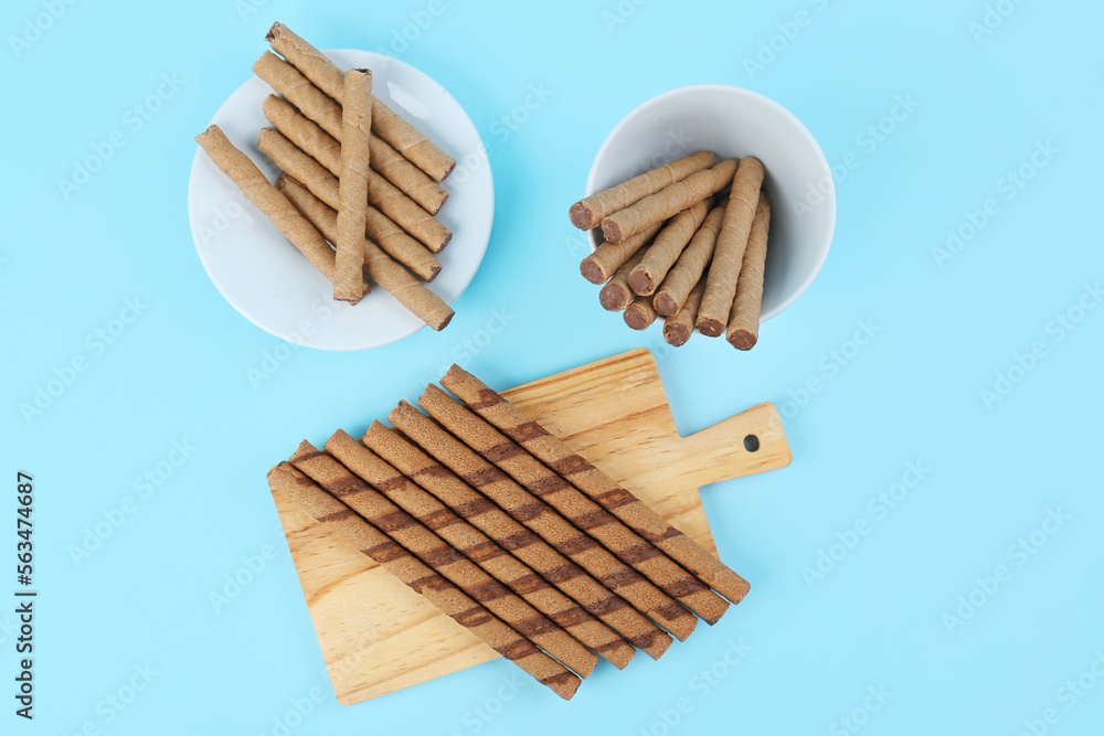 Plate, bowl and board with tasty wafer rolls on blue background