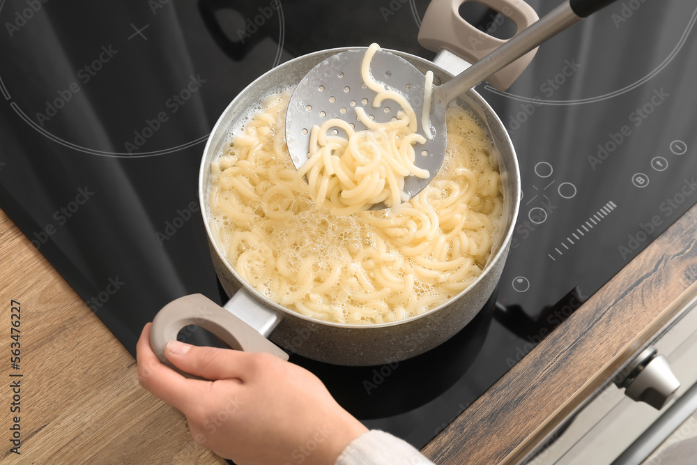 Woman cooking tasty pasta on stove in kitchen, closeup