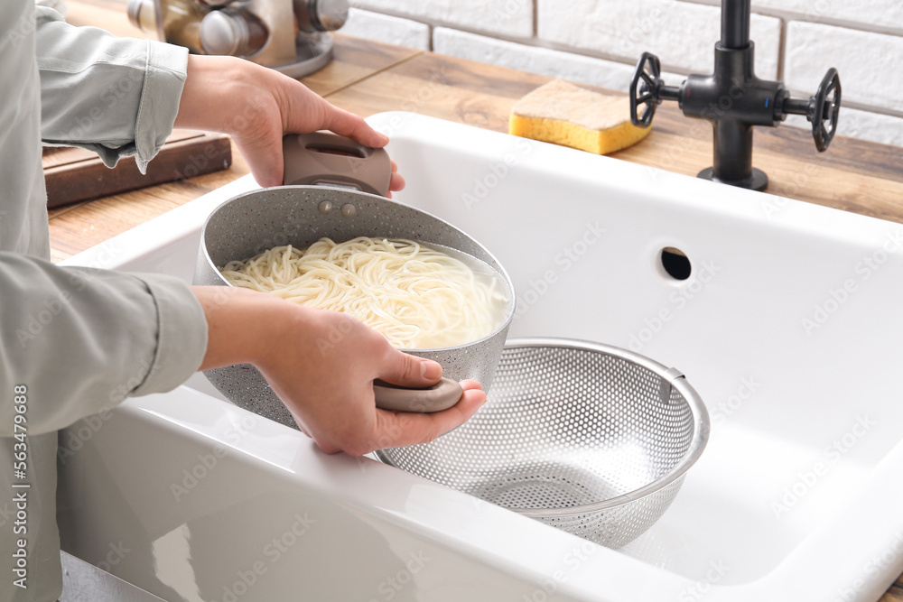 Woman pouring water from boiled pasta over sink in kitchen