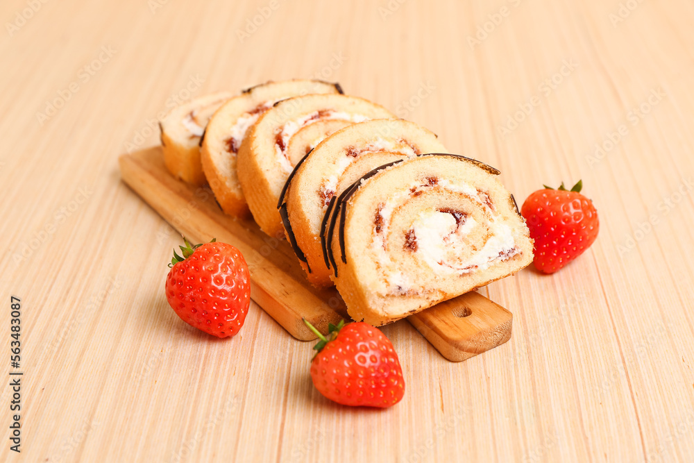 Cutting board with tasty pieces of sponge cake roll and strawberry on wooden background