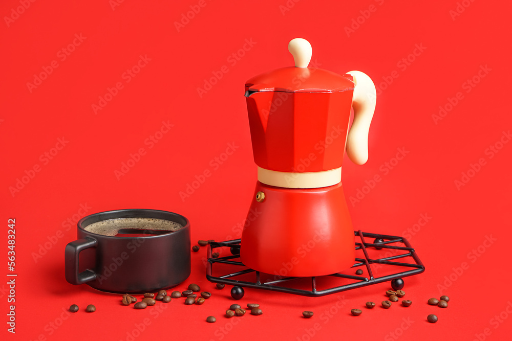 Metallic board with geyser coffee maker, cup and beans on red background