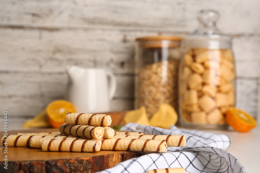 Cutting board with tasty wafer rolls and kitchen towel on table