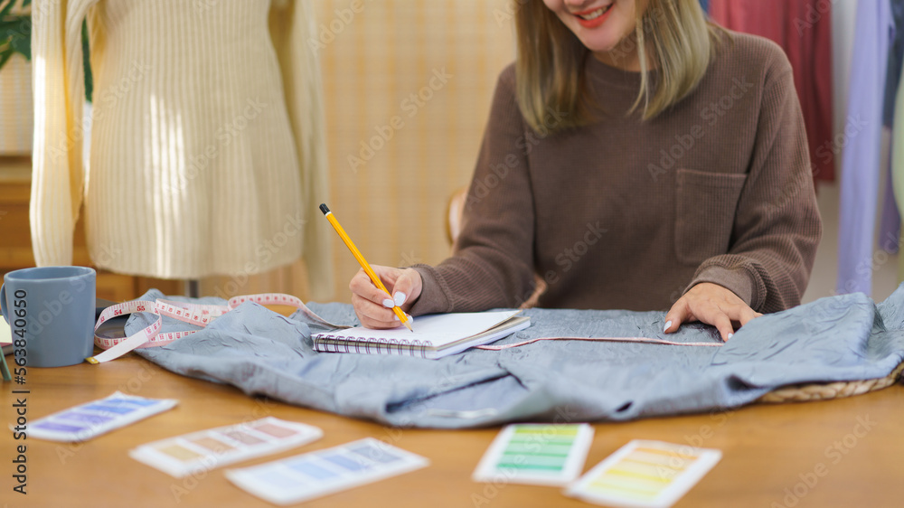 Fashion design concept, Fashion designer measuring size of shirt and taking notes data in notebook