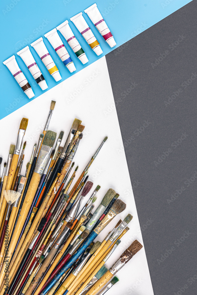 Brushes for drawing and paint on paper colored background, flat lay.