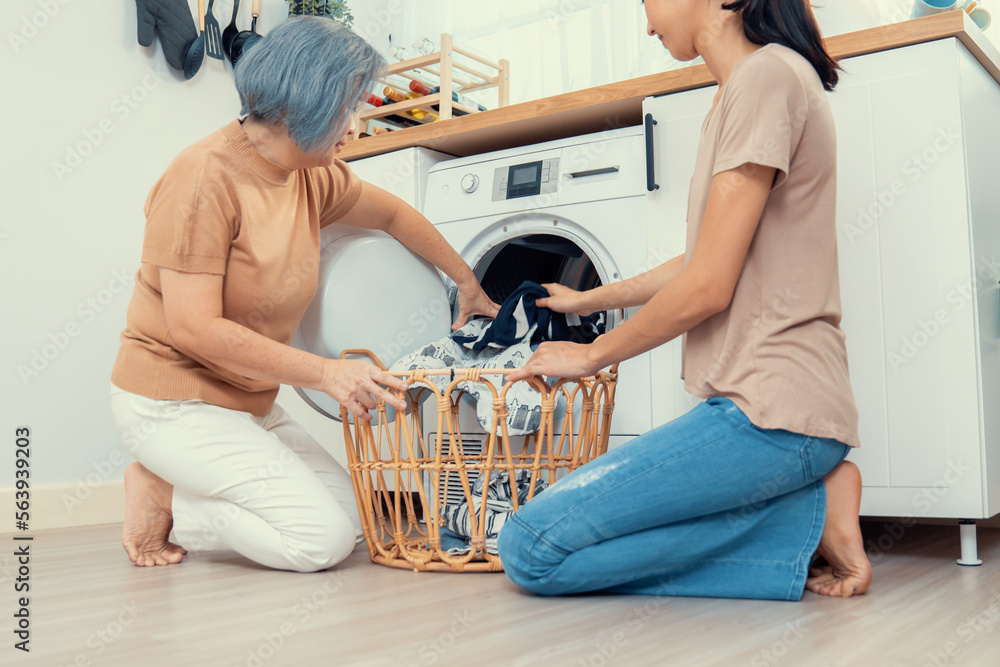 Daughter and mother working together to complete their household chores near the washing machine in 