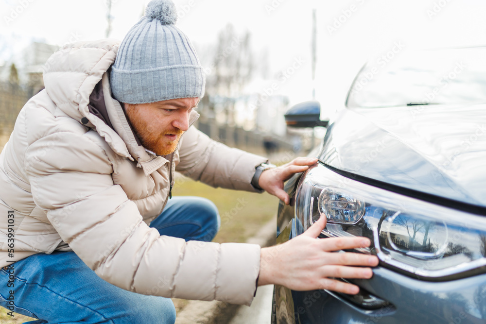 Examining the damage a man looks at a car with scratches,