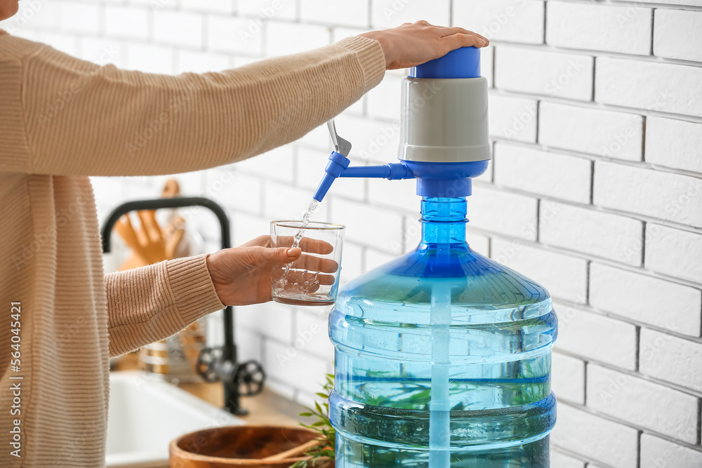 Woman pouring clean water from bottle into glass in kitchen