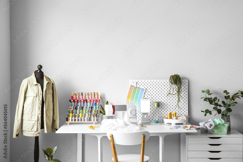 Tailors workplace with sewing machine, pegboard and tablet computer in atelier