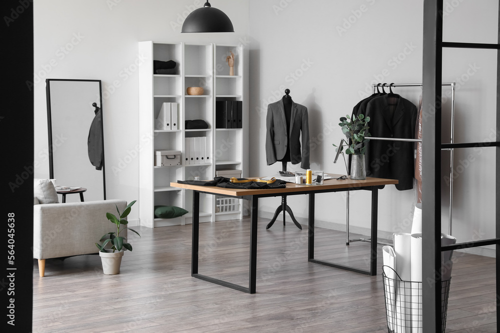 Interior of modern atelier with tailors workplace, shelving unit and clothes