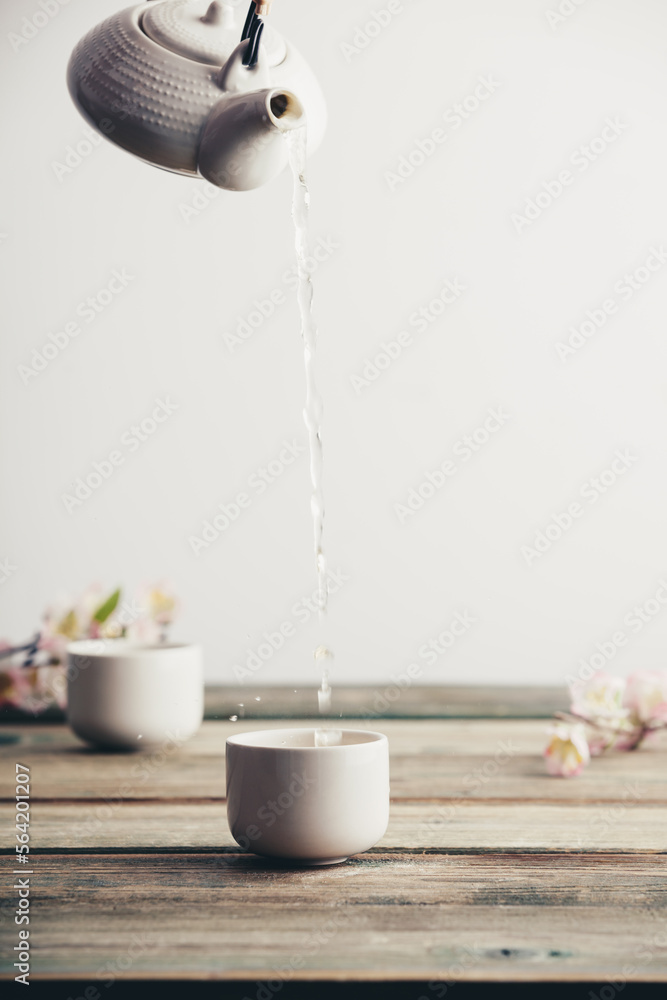 Pouring hot tea into porcelain cup on wooden table background