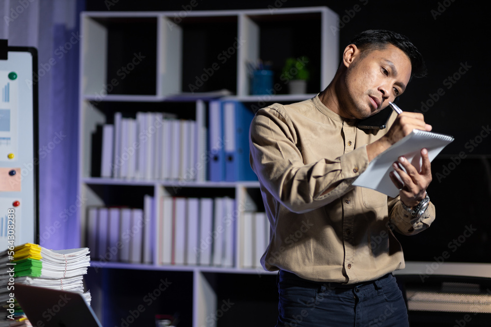 Responsible businessman working overtime in the office talking on the phone with customers.