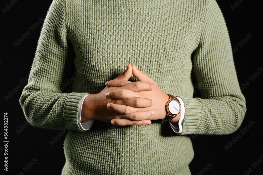 Young businessman with wristwatch on black background, closeup