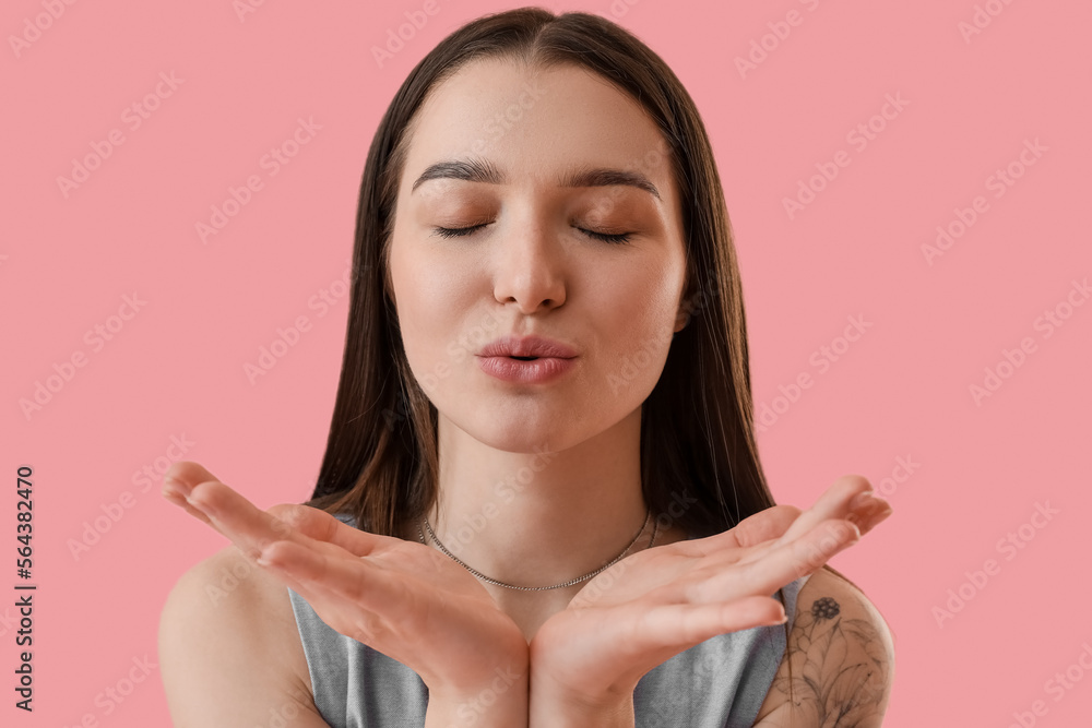 Young woman blowing kiss on pink background, closeup