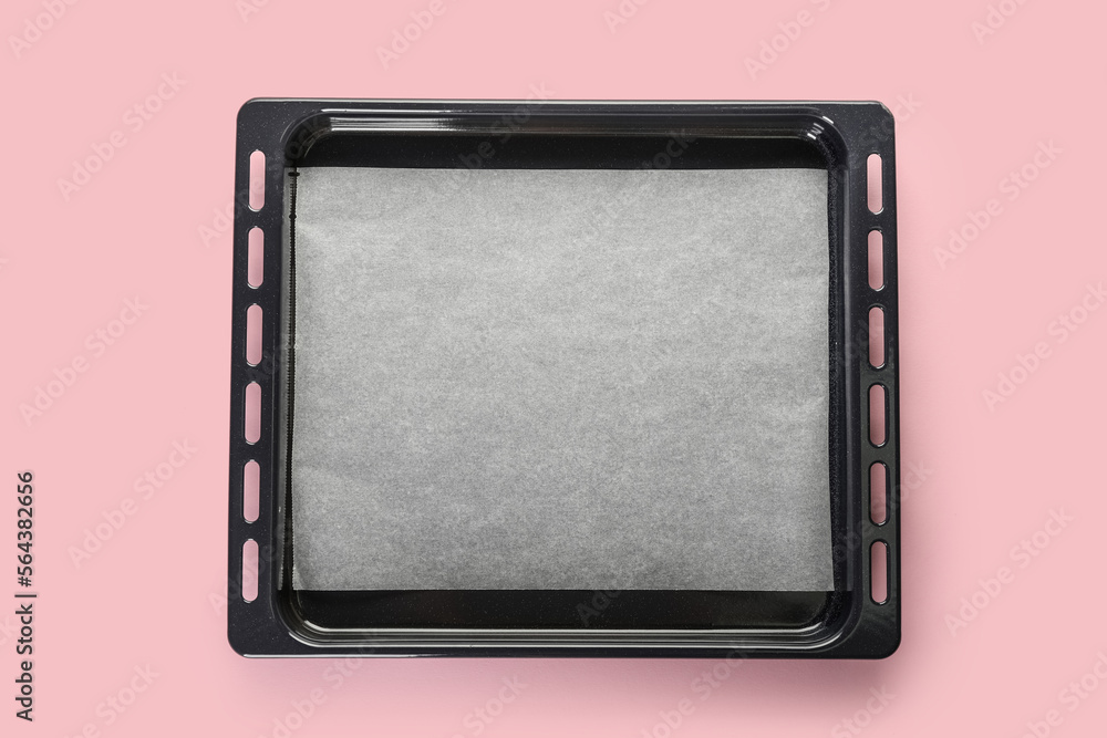 Baking tray with parchment paper on pink background