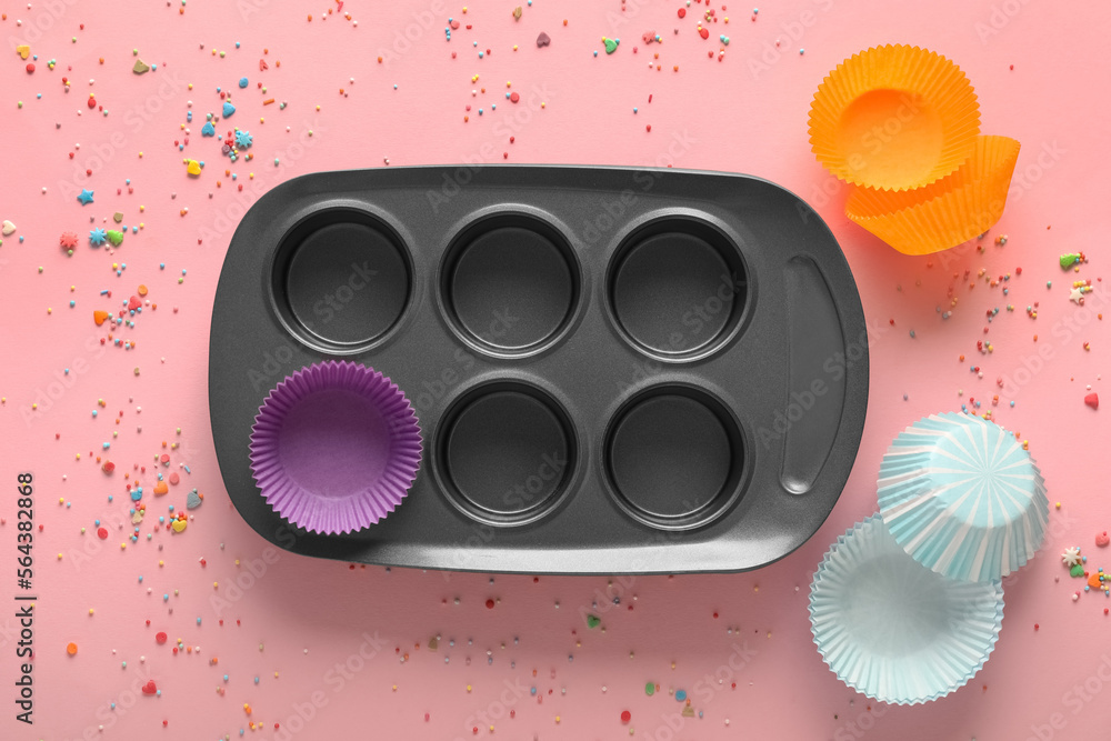 Muffin baking tray with paper forms and sprinkles on pink background