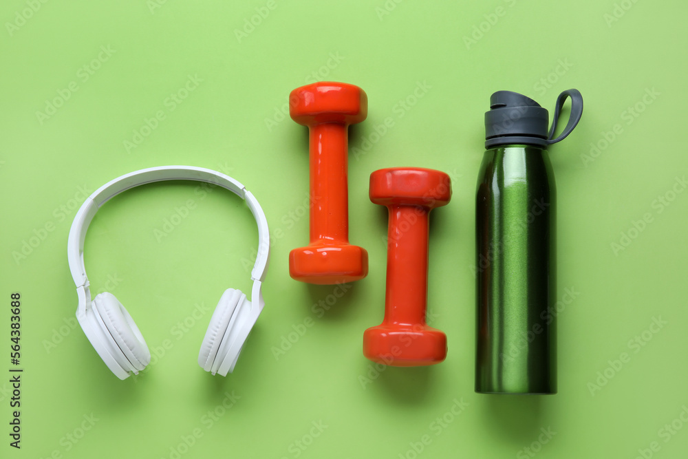 Sports water bottle with dumbbells and headphones on green background