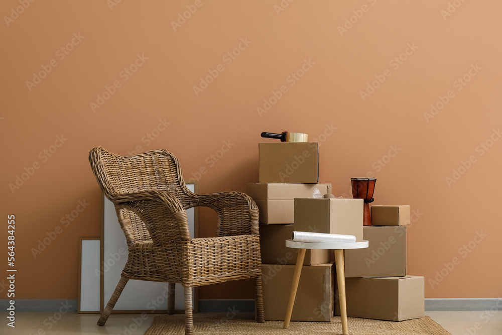 Moving cardboard boxes with table and armchair near color wall