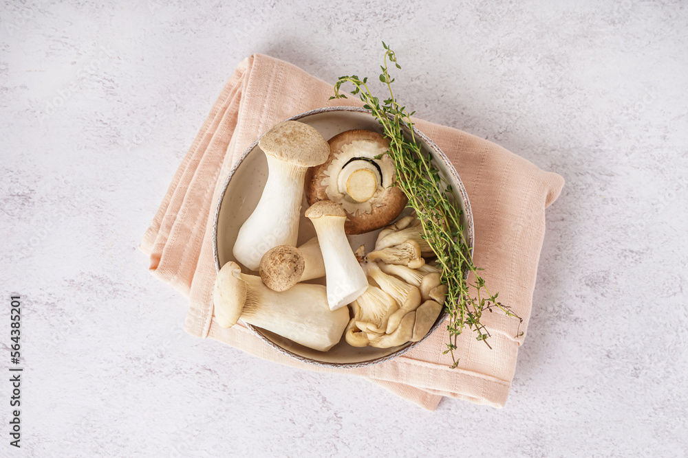 Bowl of fresh mushrooms and thyme on light background