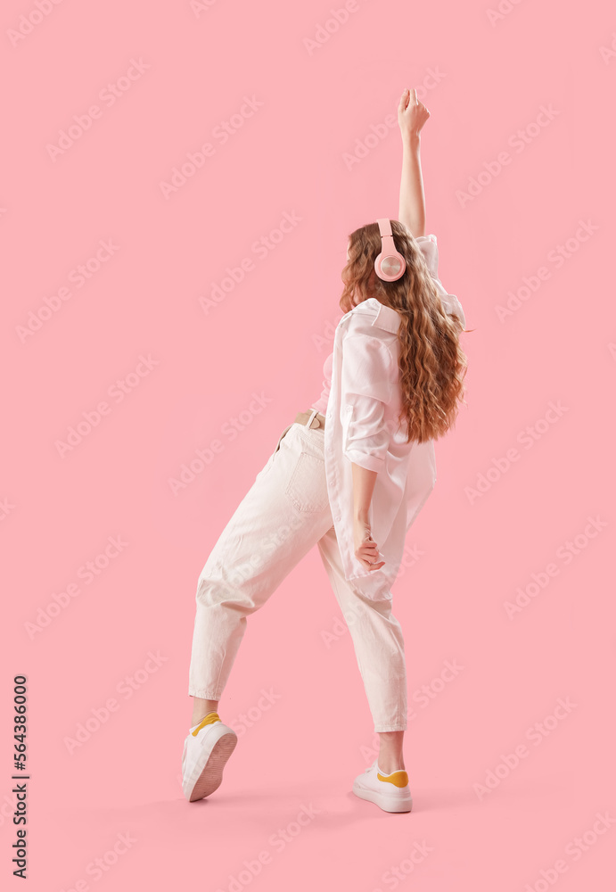 Young woman in headphones dancing on pink background