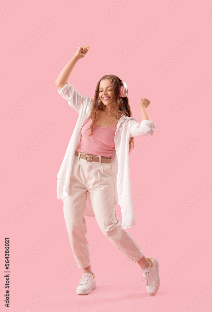 Young woman in headphones dancing on pink background