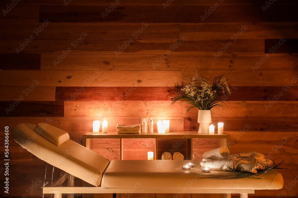 Interior of dark spa salon with couch, shelving unit and burning candles