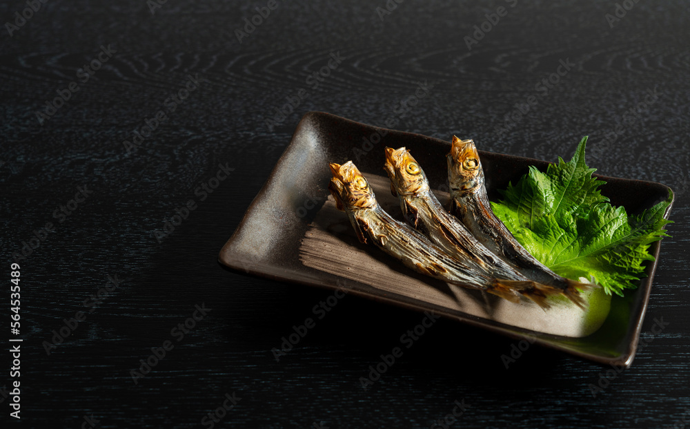 Grilled urume sardines on a black table. A side dish of sake.