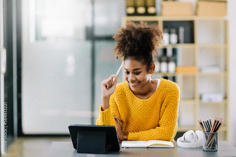 Attractive young African student studying at the college library, sitting at the desk, using a lapto