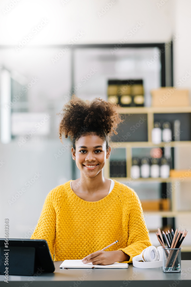 Attractive young African student studying at the college library, sitting at the desk, using a lapto