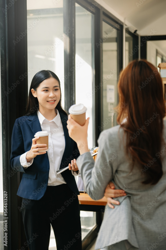 Happy two Asian business woman holding coffee cup in coworking office.