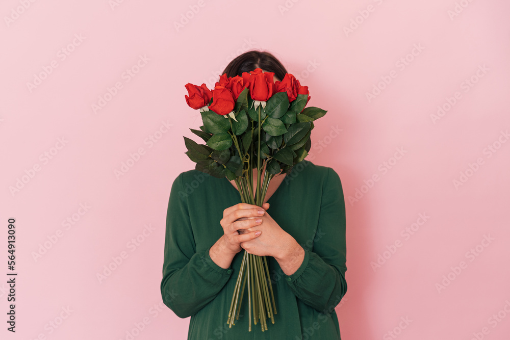 Lady with bouquet of red roses against pink background.