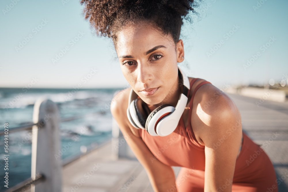 Portrait, fitness and black woman tired, ocean and runner with headphones, focus and determined for 