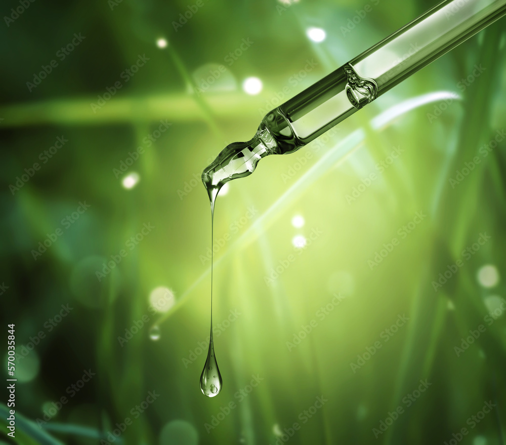 Cosmetic pipette with drop close-up on a blurred natural background with bokeh