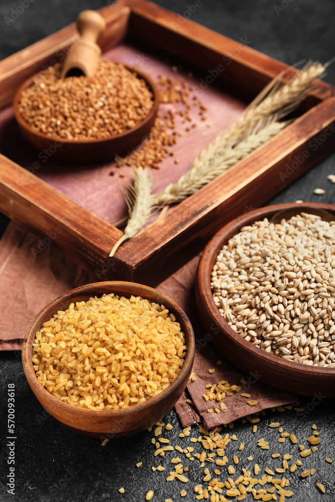 Bowls with pearl barley and bulgur on dark background, closeup