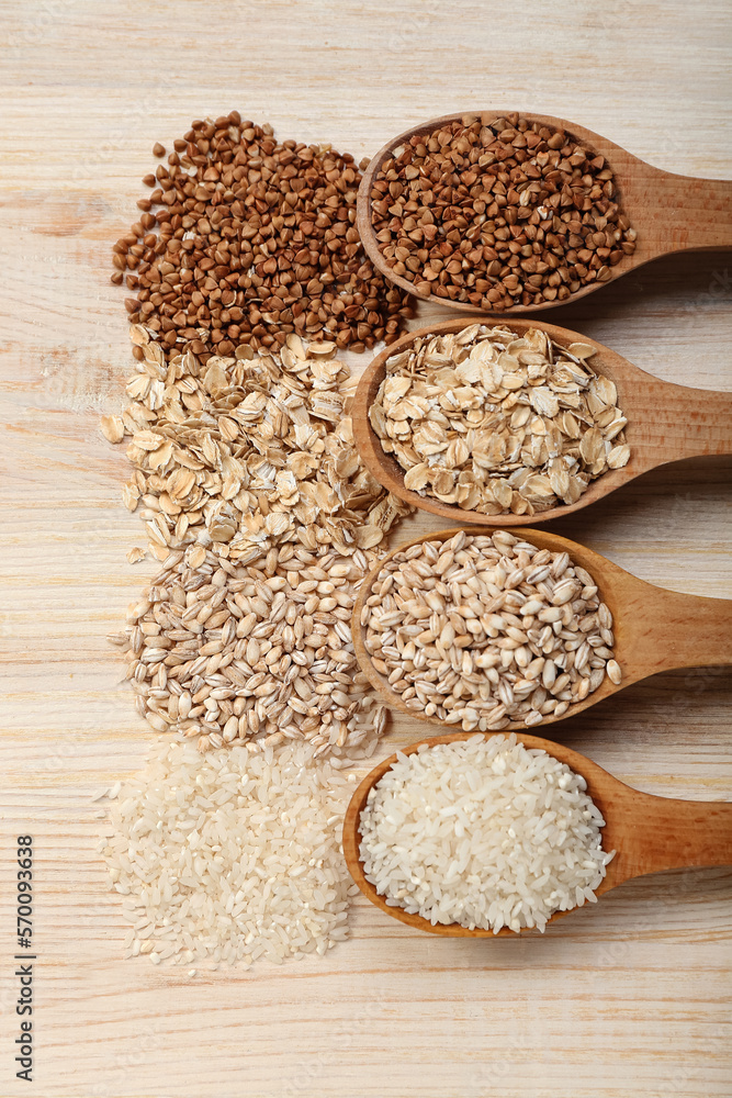 Spoons with different cereals on wooden background, closeup