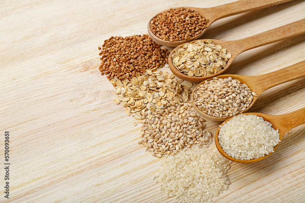 Spoons with different cereals on wooden background