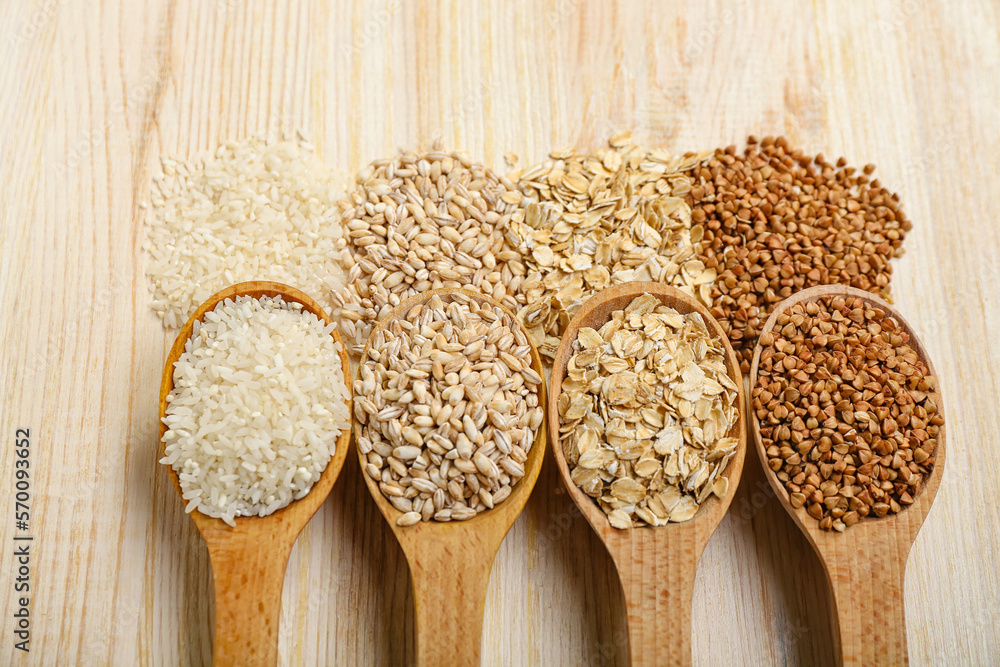 Spoons with different cereals on wooden background, closeup