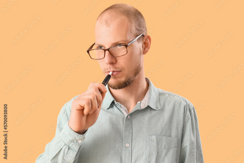 Young man in eyeglasses smoking disposable electronic cigarette on beige background