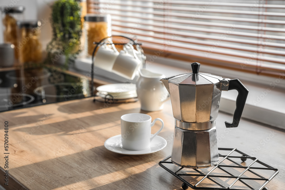 Grid with geyser coffee maker and cup on kitchen counter near window