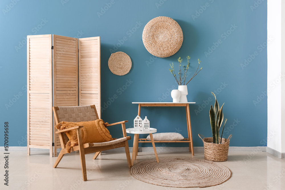 Interior of living room with armchair and house candle holders on table near blue wall