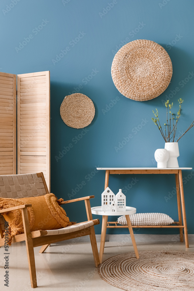 Interior of living room with armchair and house candle holders on table near blue wall