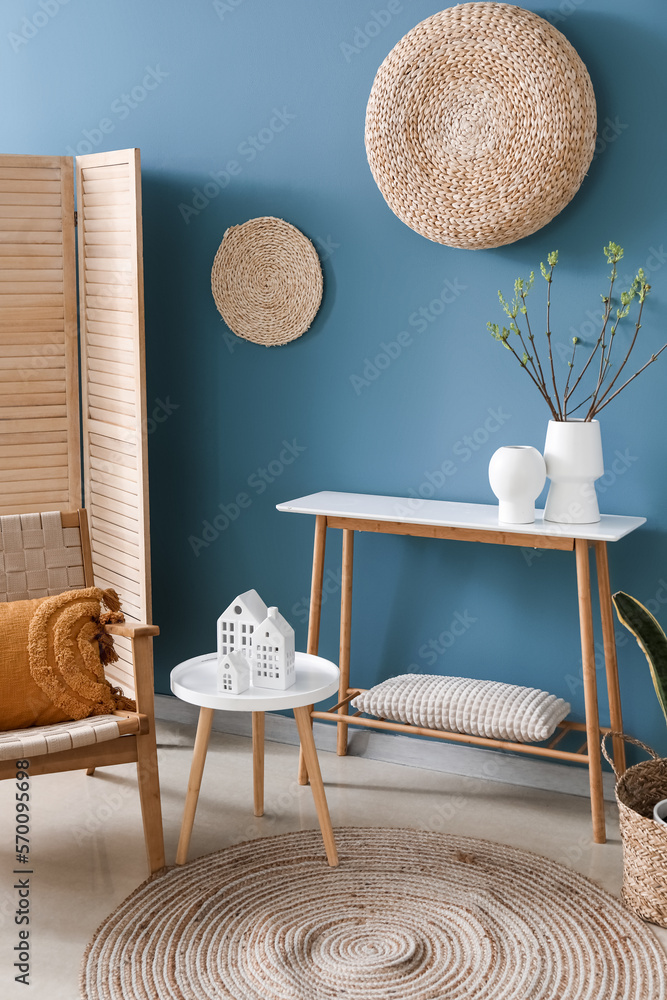 Interior of living room with house candle holders and houseplant on table near blue wall