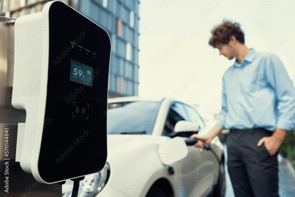 Focus public EV charging station in city residential area with blur background of businessman chargi