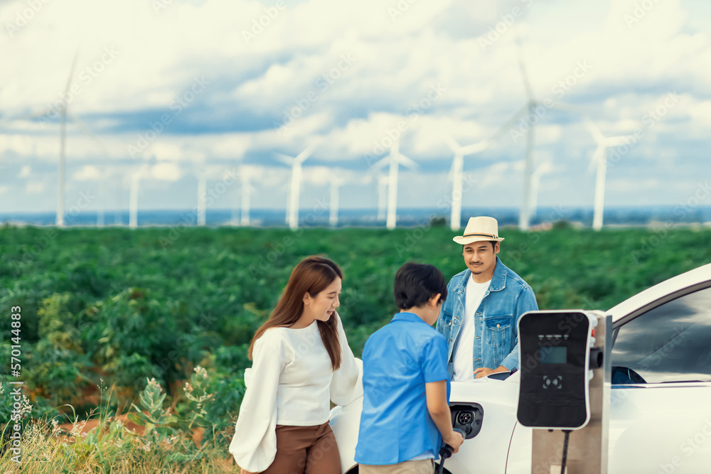 Concept of progressive happy family enjoying their time at wind farm with electric vehicle. Electric