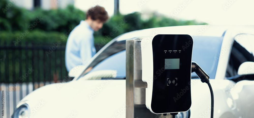 Focus public EV charging station in city residential area with blur background of businessman chargi