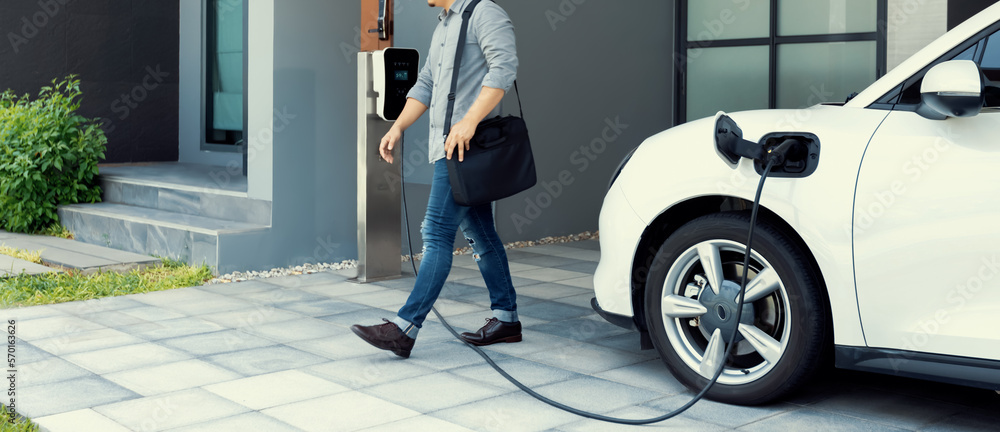 Progressive asian man and electric car with home charging station. Concept of the use of electric ve