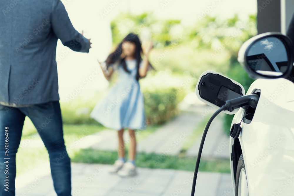 Progressive father and daughter plugs EV charger from home charging station to electric vehicle. Fut